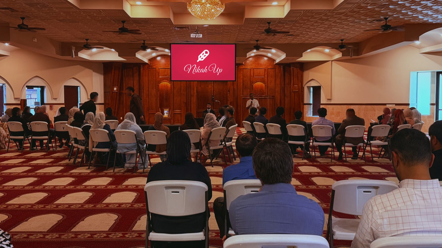 The banquet hall at Maryam Islamic Center from the back, rows of seats facing the NikahUp screen.